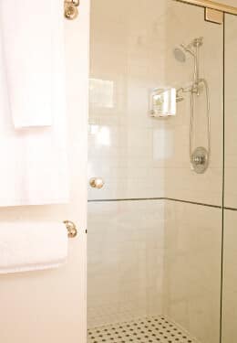 Cream tiled shower with glass door, towel racks hanging on cream wall