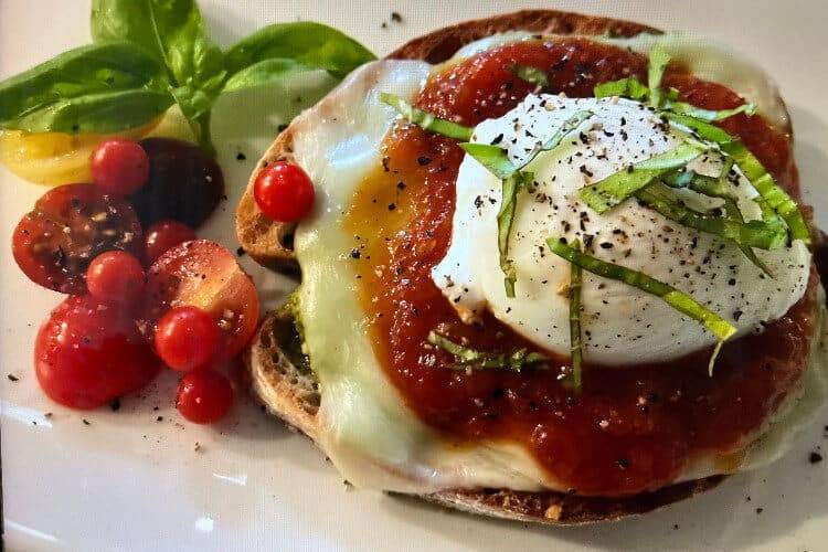 Eggs Benedict on toasted muffin on white plate with serving of cherry tomatoes