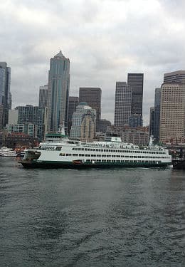 White ferry boat along the river with sky scrapers in the background against a grey, cloudy sky.