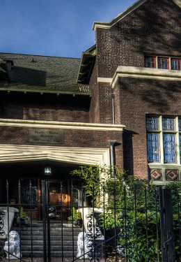 Exterior View of the inn, a brown and tan structure with green bushed in front against a blue sky