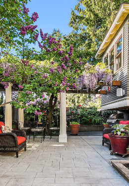 Concrete patio with red cushioned wicker furniture, pillars holding up trellis with flowers and greeneryand