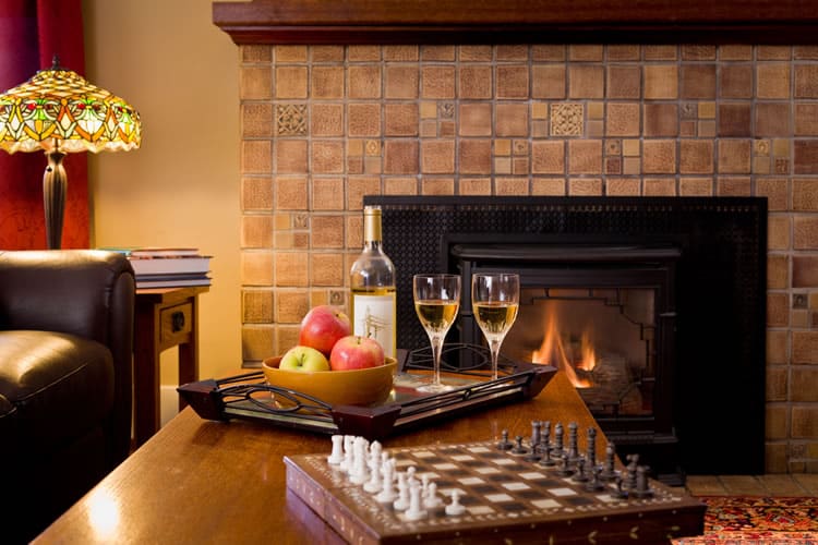 A tray of a bottle of white wine and two glasses and red and green apples sits between a chess set and a fireplace at the Greenlake Guest House.