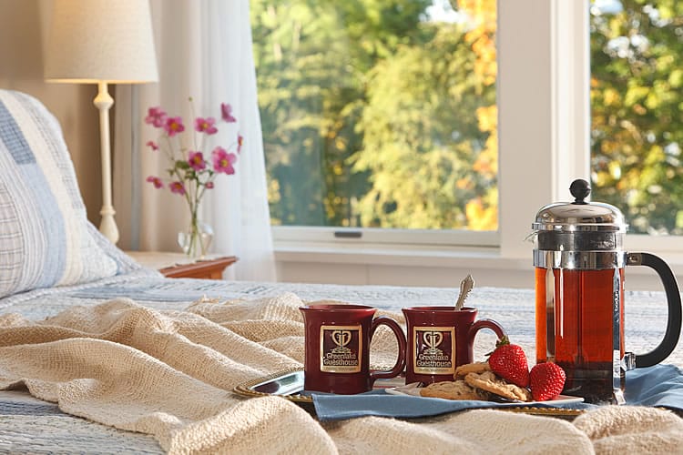 A tray of burgundy mugs and a French press coffee set sits on a bed at the Greenlake Guest House.