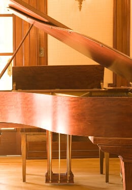 Brown wooden grand piano sitting on wood floor with sun reflection through window