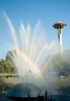 A fountain sprays before a bright blue sky and the Space Needle.