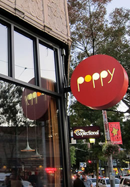 An outdoor restaurant with a red sign that reads Poppy in white and orange lettering.