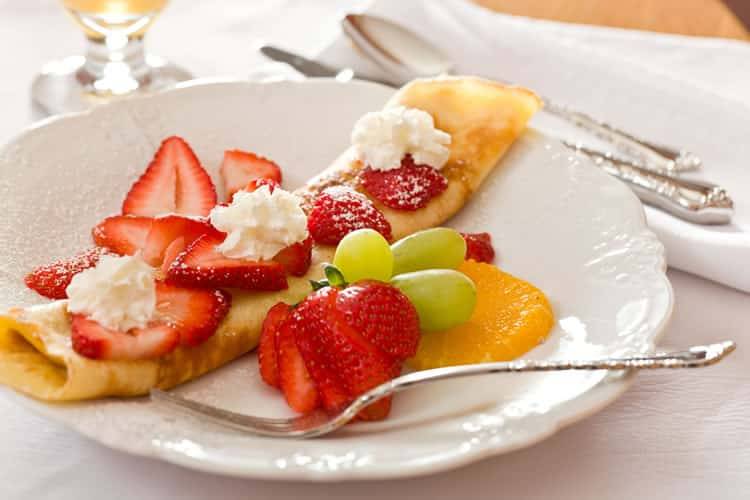 Red strawberries and green grapes sit atop a crepe on a white plate at the Greenlake Guest House.
