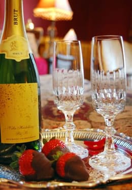 A bottle of Brut champagne sits on a silver platter with two glasses and three brown chocolate covered red strawberries.